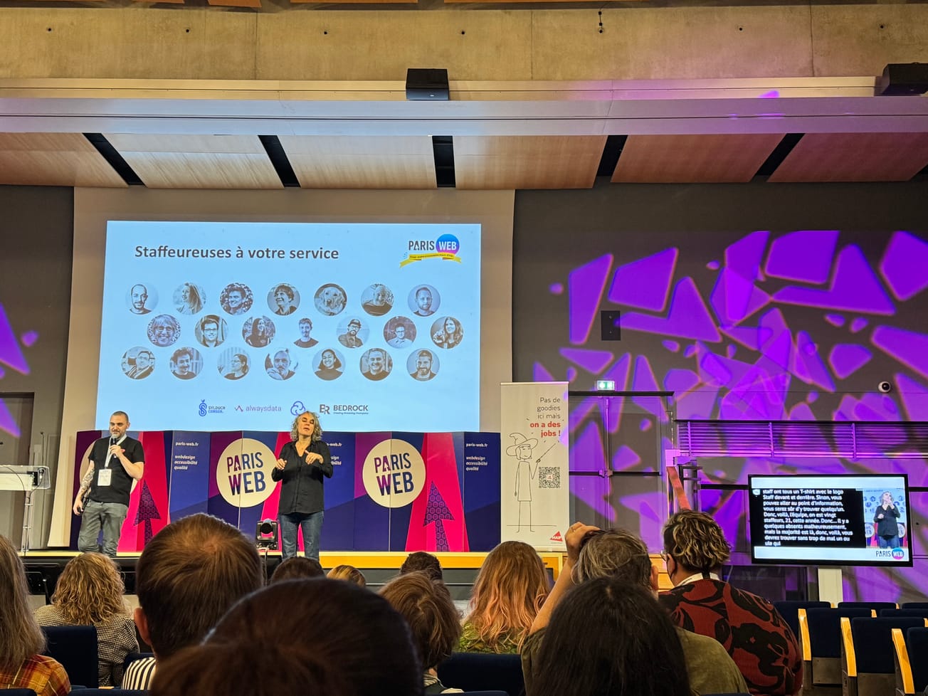 Un écran présente les photos des "Staffeureuses à votre service". Sur la droite de la scène on voit un écran affichant la retranscription en vélotypie et l'interprète LSF.